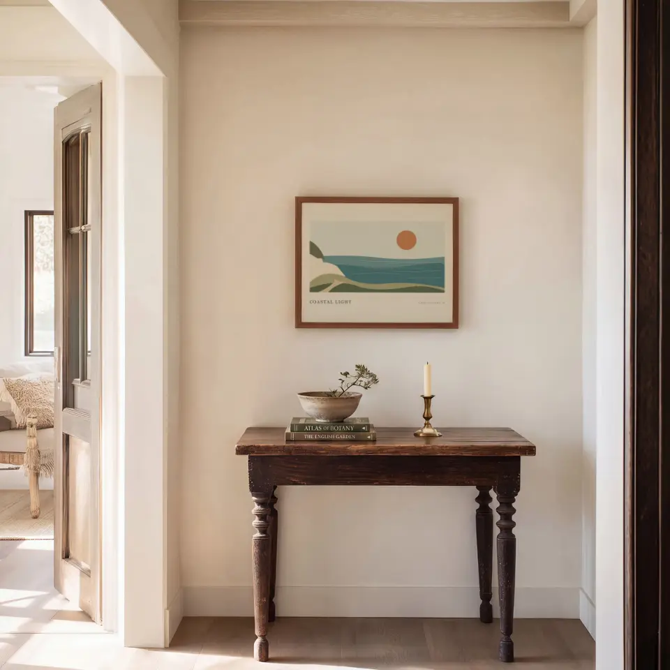 Antique Hall Console: A modest walnut frame hangs centred on a creamy plaster wall above a carved antique console table with turned legs.